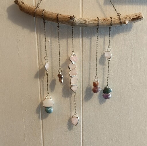 Different rocks soldered individually or together in pairs, hanging on chain from a piece of wood.