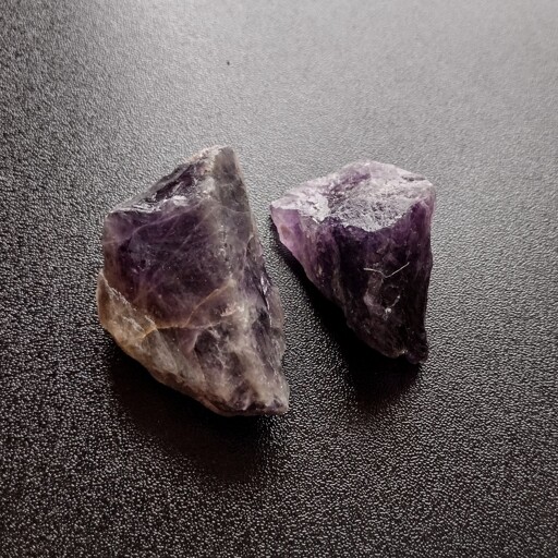 Two rough chunks of purple Amethyst on a black tabletop.
