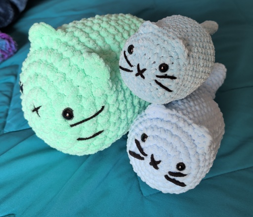 Blue / green crocheted cat plushies ontop of a blue bed.