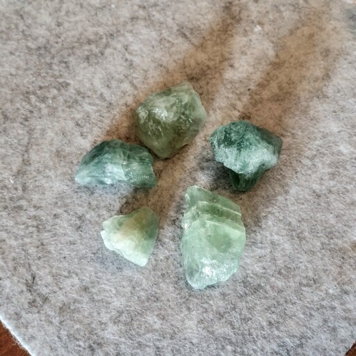 Five semi-transparent teal-coloured rough rocks sitting on a gray felt mat.