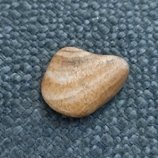 A smooth, flat, tan rock with striations of paler and darker lines.