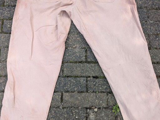 Close-up view of the articulated knee section of a pair of tan, avocado-dyed cotton pants laid out on brick paving.