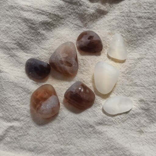 An image of five smoothed out smokey quartz and three white quartz rocks on a white towel.