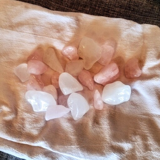 About two dozen, or a couple handfuls of white quartz and rose quartz stones, semi-smooth and wet, on a white cloth.